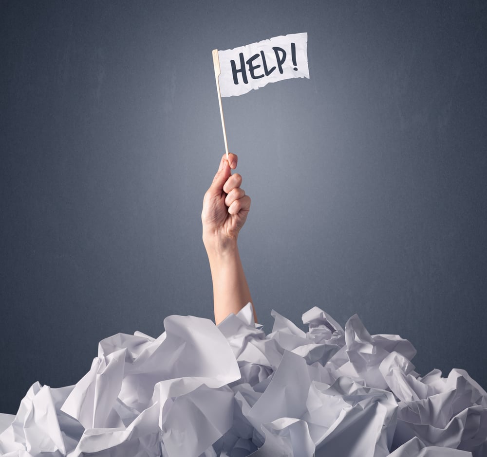 Female hand emerging from crumpled paper pile holding a white flag with help written on it